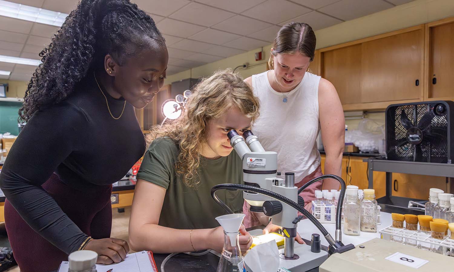 3 students look at microscope