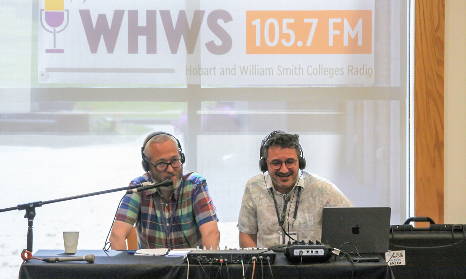 The hosts sit at a table with mic equipment