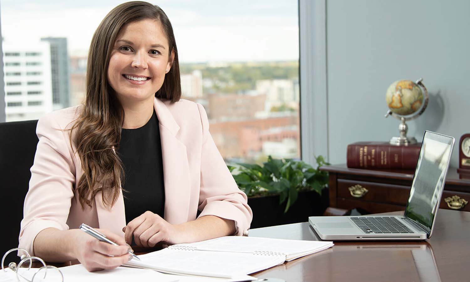 Sarah O'Brien smiling and holding a pen at a desk with an open laptop