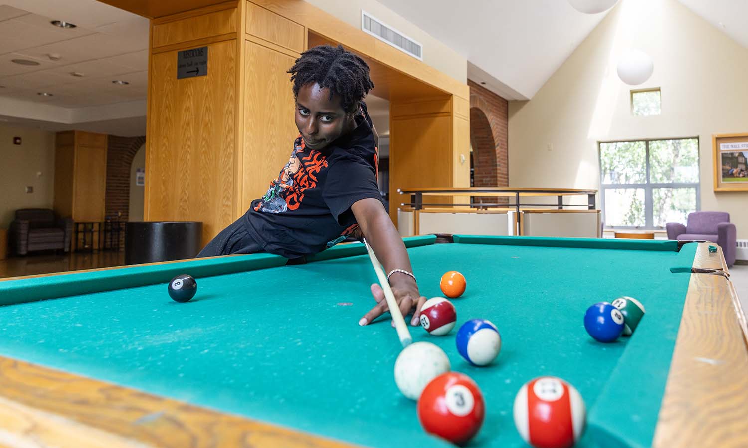 In the Scandling Campus Center, Chris Njomo ’28 enjoys playing pool with friends, as it reminds him of playing back home in Kenya. 