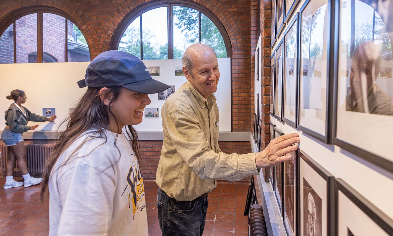 Júlia Accioly '26 helps Neil Sjoblom ’75 hang photos taken by alumni in the Solarium Gallery at Houghton House before the beginning of Reunion.