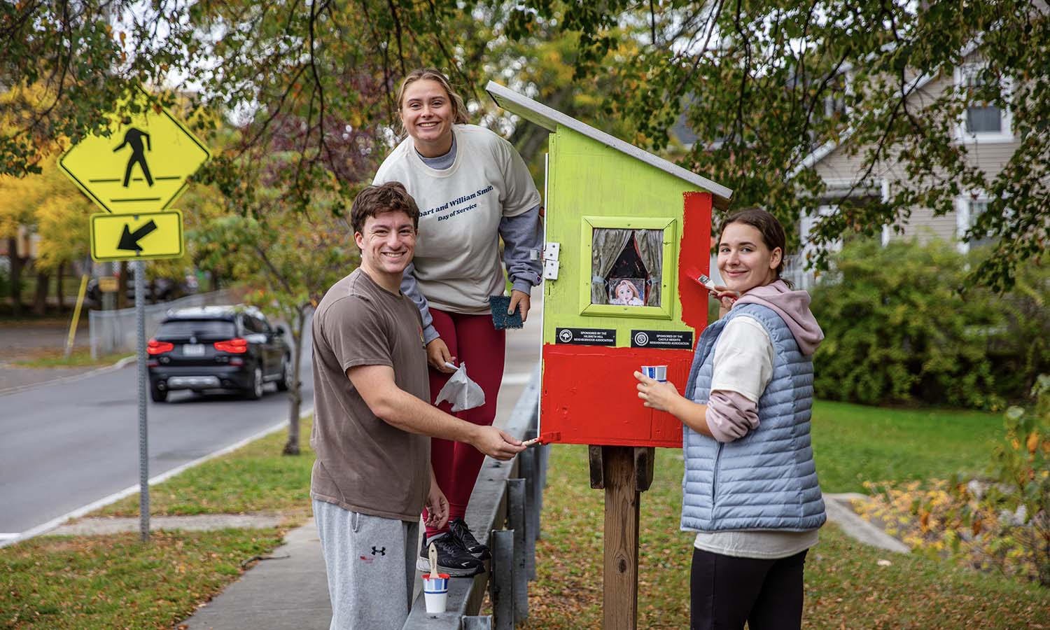 At Brook Street Park, Leyton Demeo ’27, Chloe Odell ’27 and Iona University student Jess Navarrete paint a Little Free Library. 