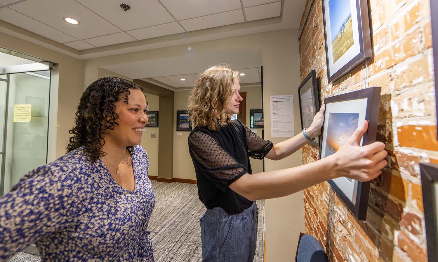 Associate Director of the Center for Global Education Colleen Kolb and Pre-departure and Re-entry Programming Coordinator Hannah Mathews hang the winning photos from the study abroad photo contest in Trinity Hall. 