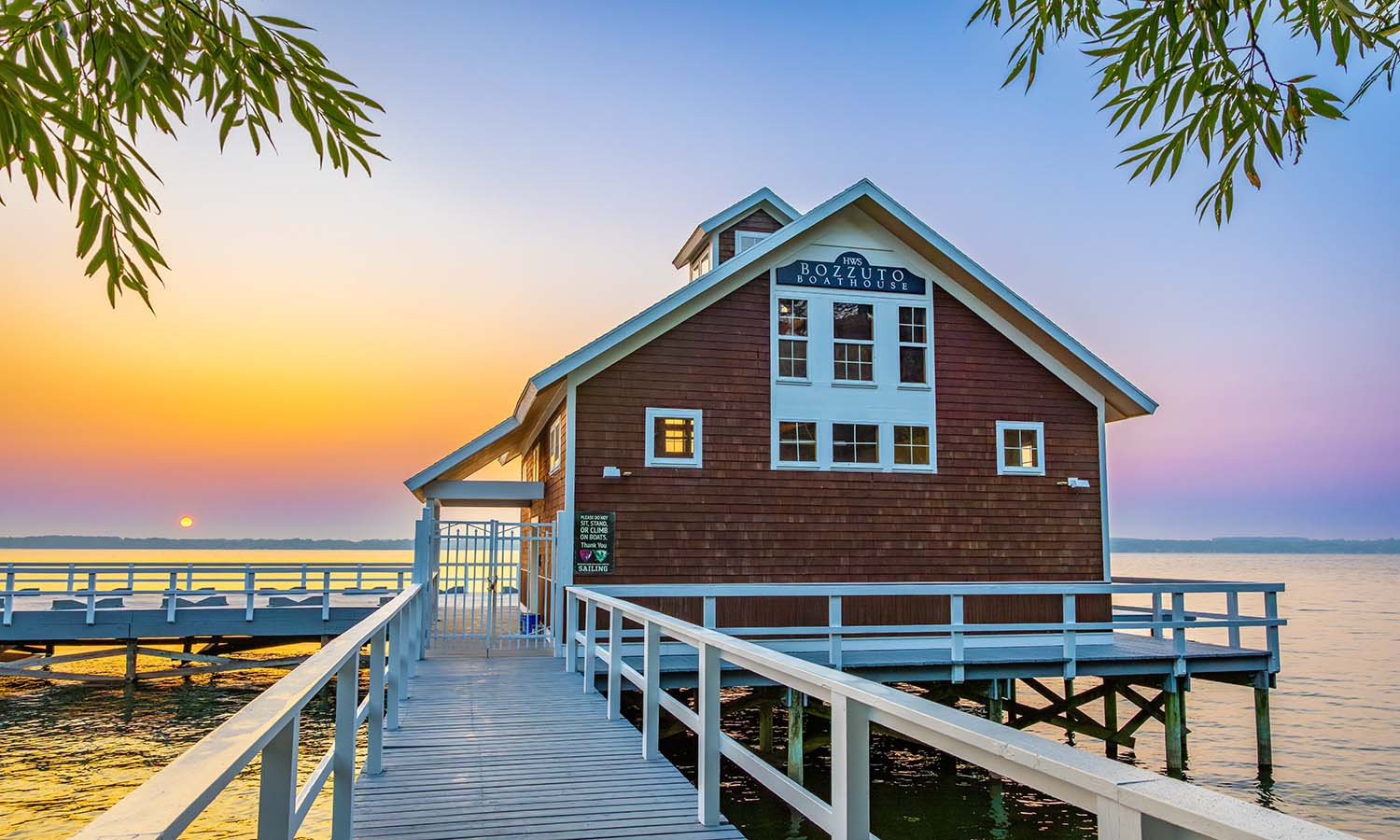 The sun rises above Seneca Lake and Bozzuto Boathouse. 