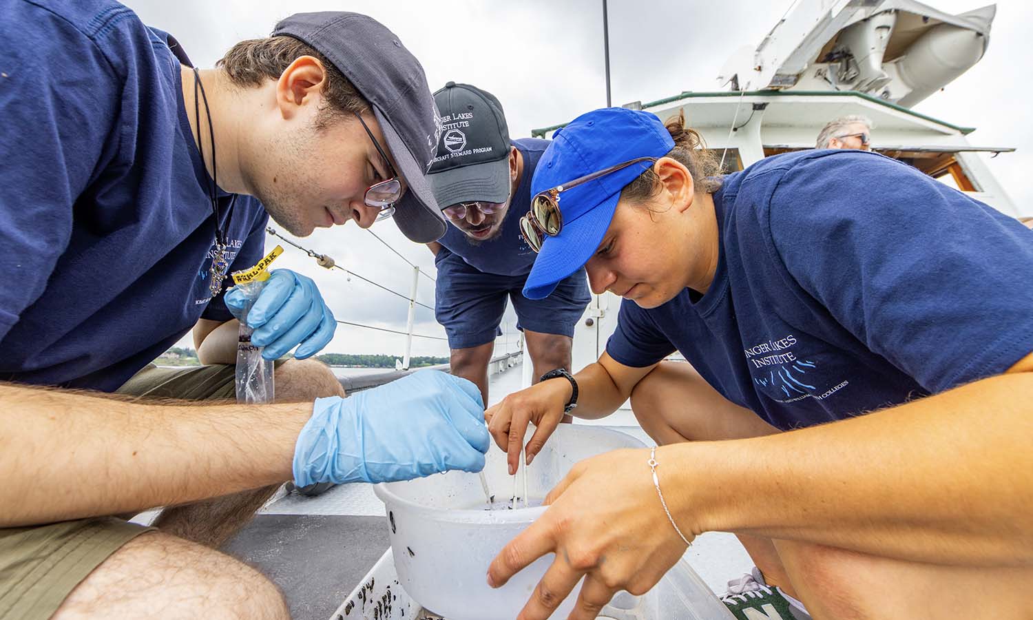 Aquatic Invasive Species Technician Sam Lubell, Daudi Aden ’26 and Linnea Darius ’26 collect organisms from the sediment of Seneca Lake for stable isotope analysis to help characterize the aquatic food web of the lake. 