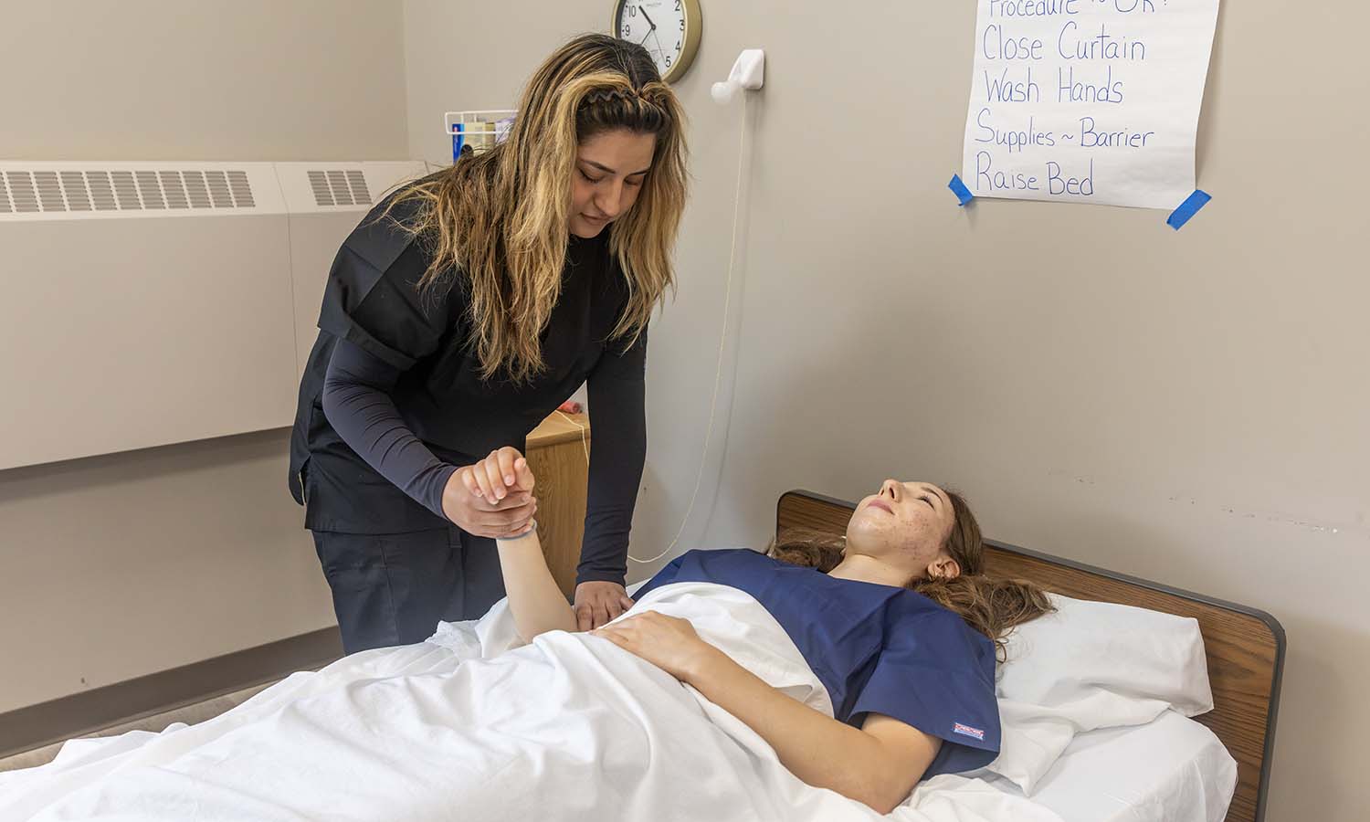 Kayla Mosqueda ’27 practices taking the pulse of Amalia Olivieri ’28. Both completed coursework at Finger Lakes Community College this summer to become Certified Nursing Assistants. 