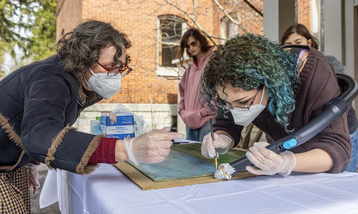 Outside of Houghton House and wearing masks and gloves to follow appropriate conservation practices, Associate Professor of Art and Architecture Liliana Leopardi works with Azure Sage ‘27 on the restoration of a painting during “Collections Management.” 