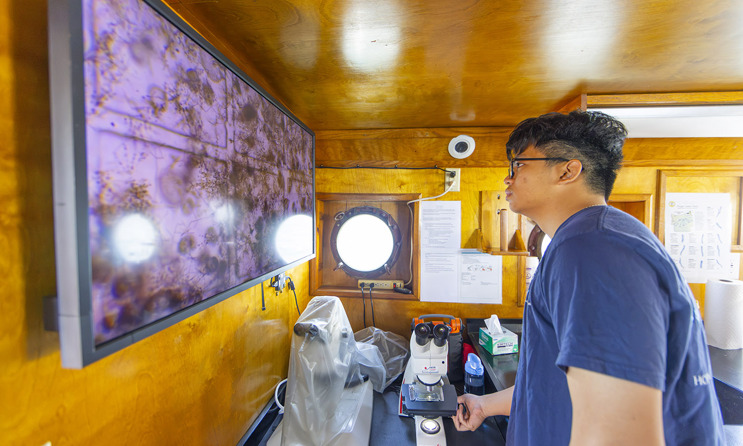 Working with researchers at HWS’ Finger Lakes Institute, Khanh Phan ‘29 examines the organisms in a water sample from Seneca Lake while on board the William Scandling aquatic research vessel. 