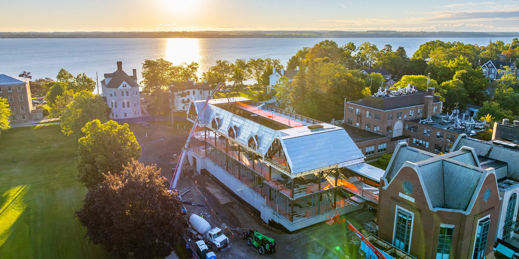 Aerial view at sunrise of the Fish Center for the Sciences under construction on the Quad, with Seneca Lake behind it