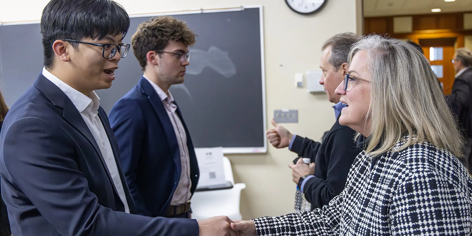 A student in a blazer shaking hands with an alumna at an HWS networking event
