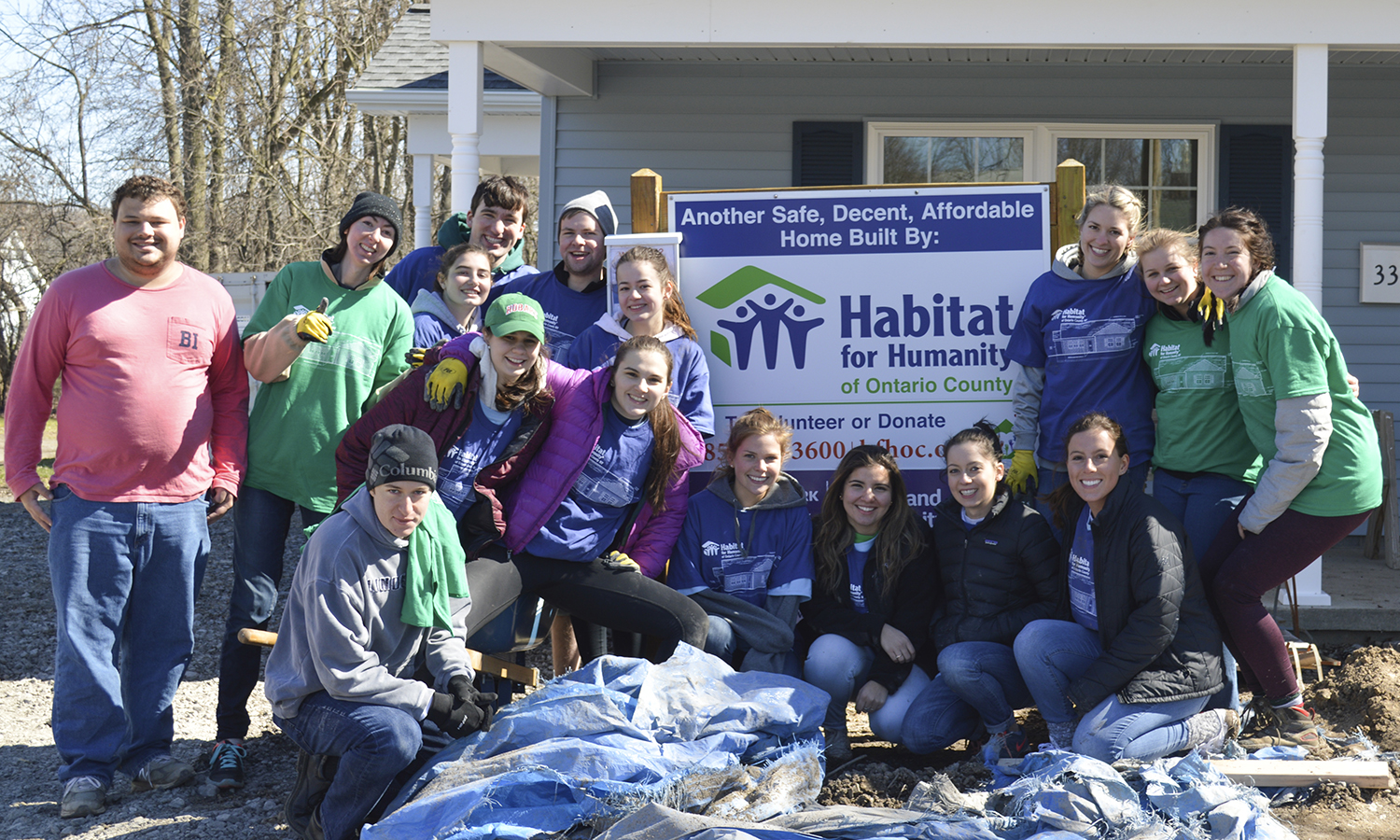 Students on a worksite gather around the Habitat for Humanity sign